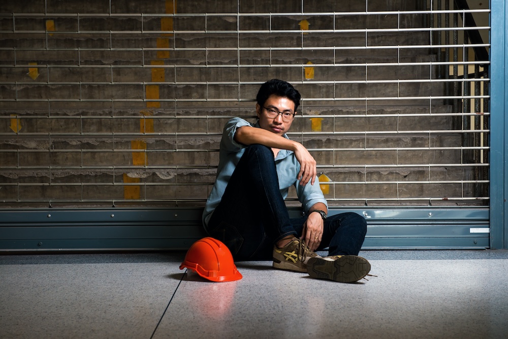 A young worker sits at the bottom of a stairwell, looking sad and tired.