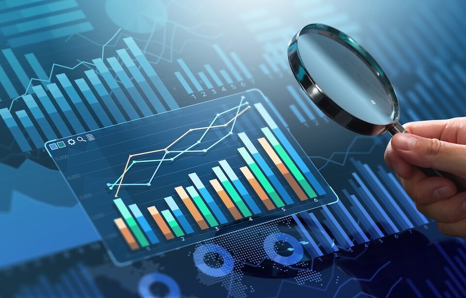 A person holds a magnifying glass over the dashboard of reports and statistics.